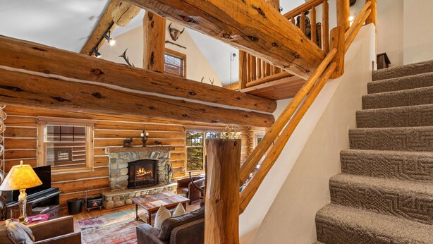 L’int érieur d’une cabane en rondins, avec une cheminée en pierre, un escalier en bois et un salon confortable doté d’un canapé et d’un téléviseur.