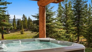 Un bain à remous installé dans un cadre naturel, surmonté d’une pergola en bois et offrant une vue sur une zone boisée.