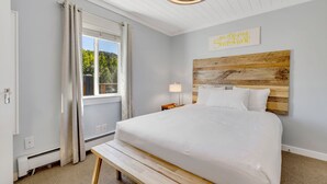 A neatly arranged bedroom with a large bed, a wooden headboard, a bedside table with a lamp, and a window with curtains. - Modern 1-Bed, 1 Bath in the Heart of Breckenridge (Breckenridge)