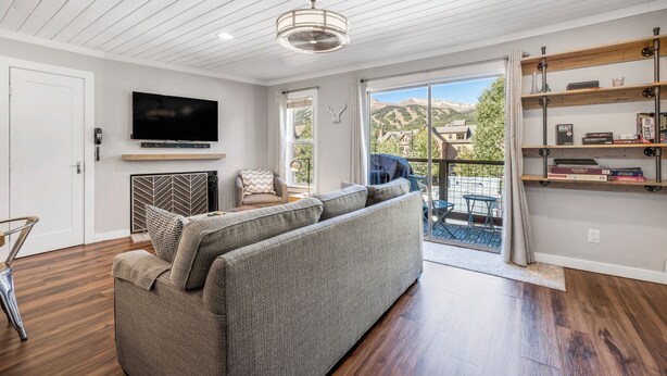 A modern living room with a grey sofa, wooden flooring, a mounted TV, and a bookshelf. - Modern 1-Bed, 1 Bath in the Heart of Breckenridge (Breckenridge)