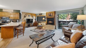 Un vaste espace de vie comprenant un salon avec cheminée, un coin repas et une cuisine dotée de meubles en bois et d’un dosseret en pierre.