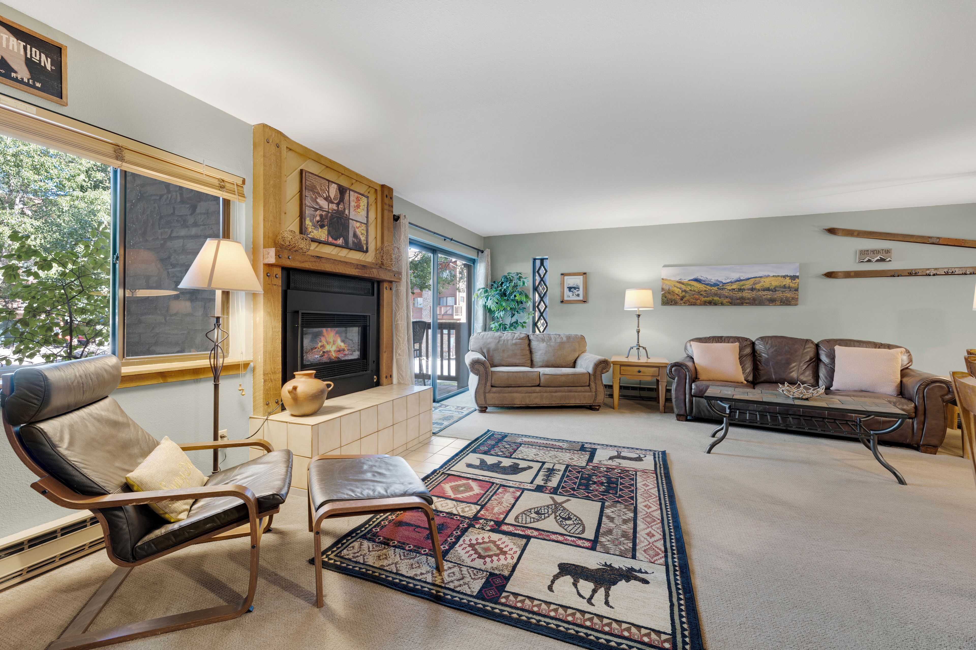 A cozy living room with a fireplace, leather sofas, a patterned rug, and a view of the outdoors.