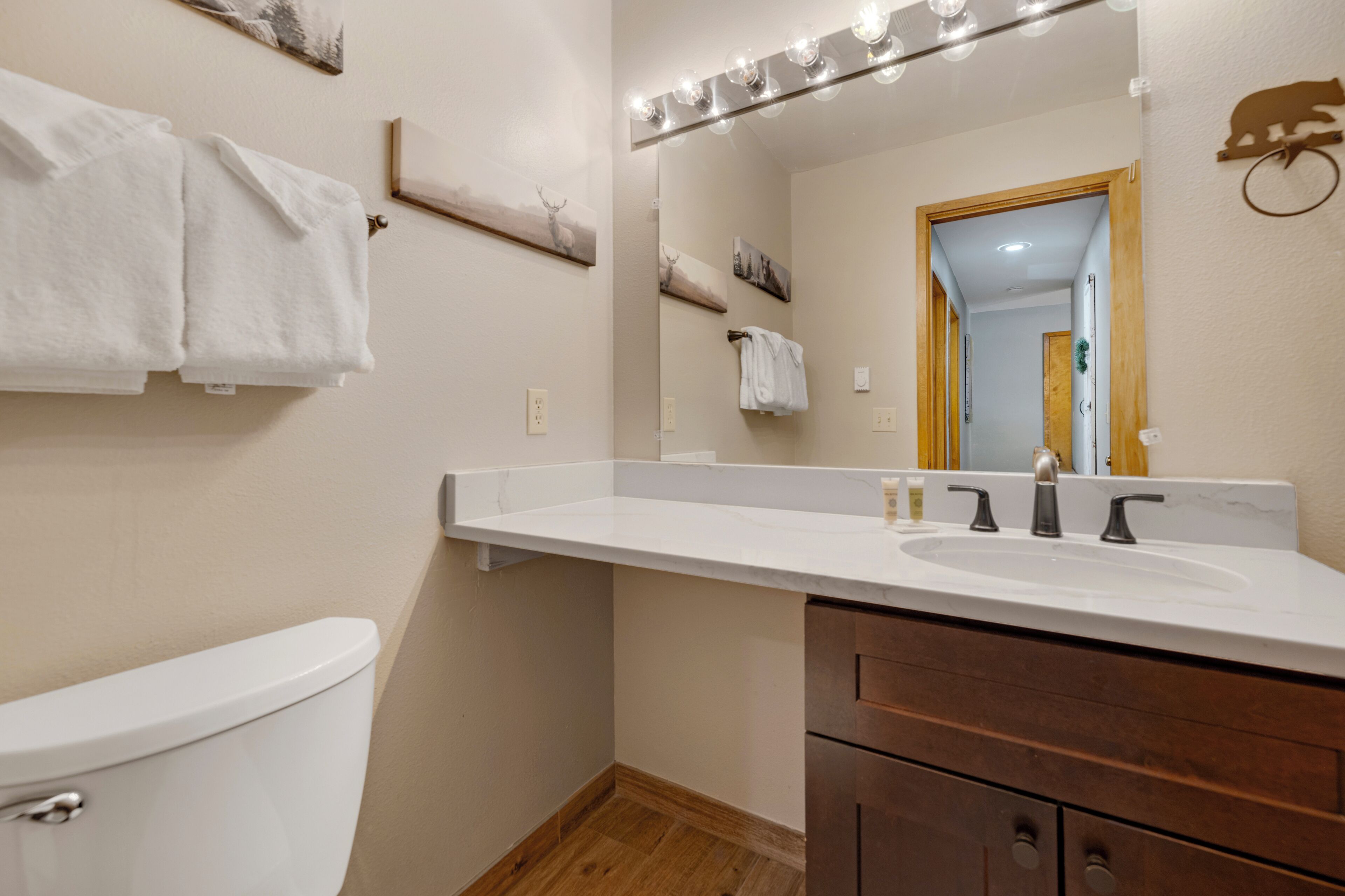 Un baño con inodoro blanco, tocador de madera con espejo y lavabo blanco.