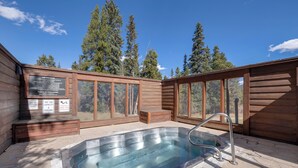 Un bain à remous aux parois en bois et aux fenêtres en verre, entouré d’arbres.