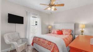 Une chambre à coucher avec un lit, une chaise, un téléviseur et un ventilateur de plafond.