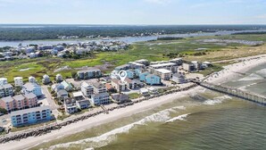 Vue aérienne d’une zone résidentielle côtière comprenant plusieurs bâtiments, une plage et une jetée.