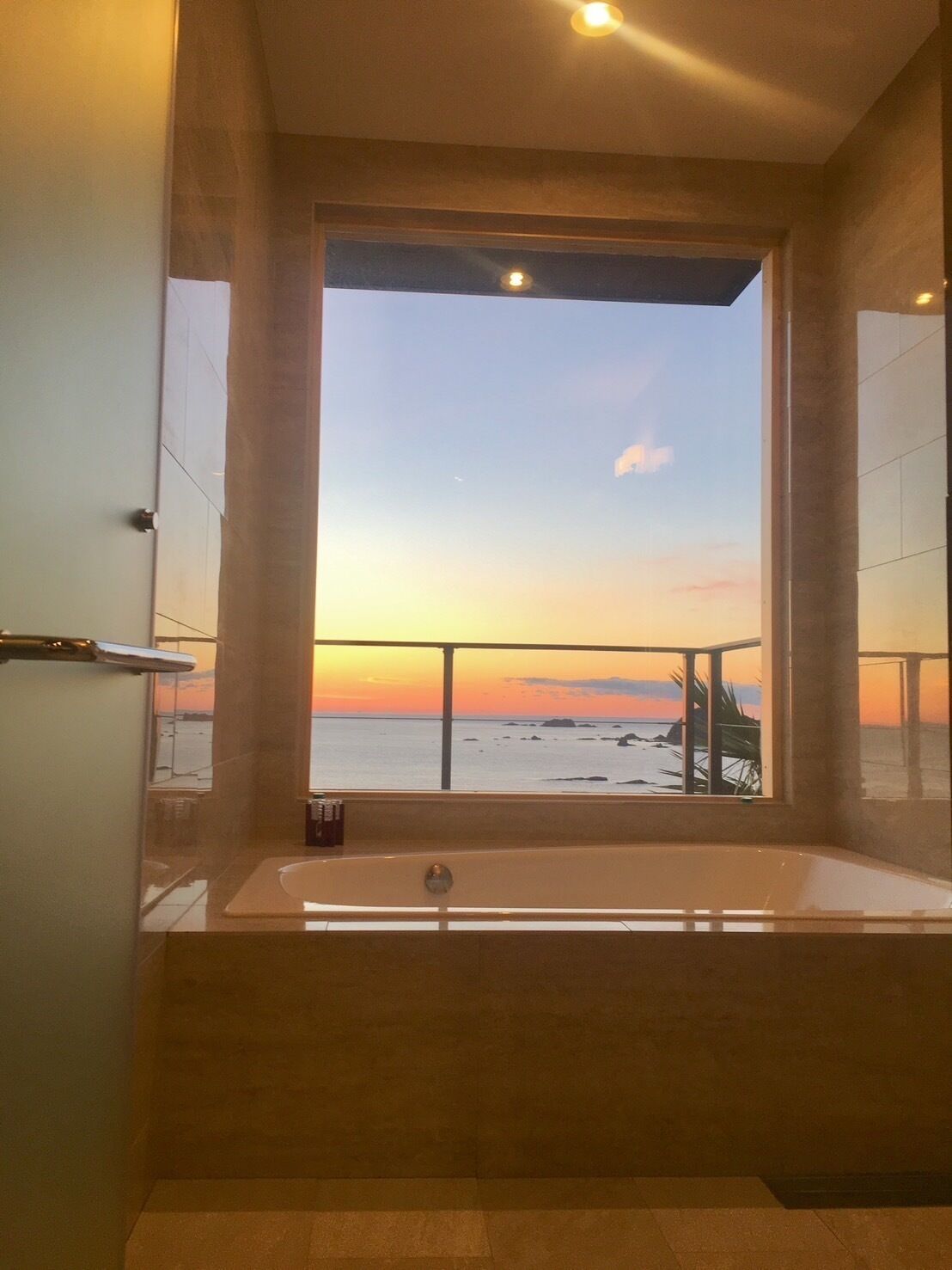 Une salle de bain dotée d’une grande baignoire et offrant une vue sur l’océan au coucher du soleil.