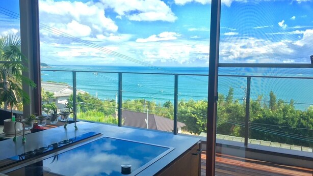 A modern kitchen with a large island, a glass top stove, and a view of the ocean through large windows.