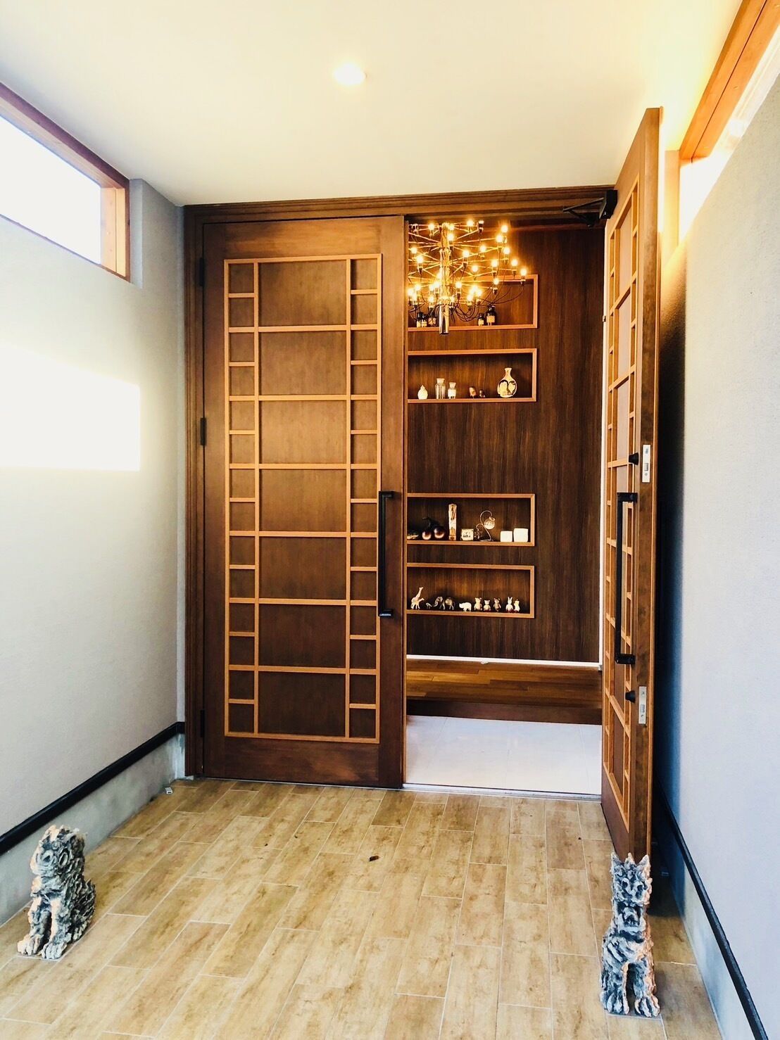 A hallway with a wooden door leading to a room with shelves and a chandelier.