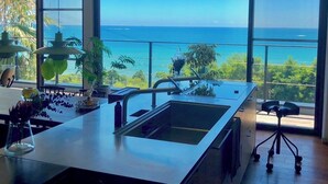 A modern kitchen with a large island, large windows, and a view of the ocean.