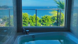 A bathroom with a large window offering a view of the ocean and greenery.