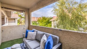 Un espacio de estar al aire libre techado con sofá y cojines, una mesita y vistas del barrio circundante.