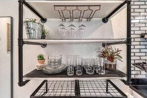 Una cocina con un estante metálico negro que contiene cristalería y plantas en macetas.
