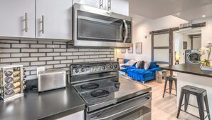 Una cocina moderna con microondas, estufa y tostadora integrados. En el área de estar contigua, hay un sofá azul.