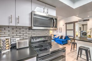 Una cocina moderna con microondas, estufa y tostadora integrados. En el área de estar contigua, hay un sofá azul.
