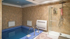 A bathroom with a stone wall, a glass shower enclosure, and a blue-tiled pool area. - Villa Kali Nadyrova (Almaty)