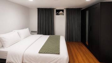 A bedroom with a bed, dark curtains, a black wardrobe, and a small wall-mounted picture.