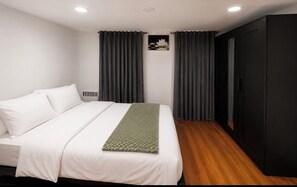 Ein Schlafzimmer mit einem Bett, dunklen Vorhängen, einem schwarzen Kleiderschrank und einem kleinen Bild an der Wand.