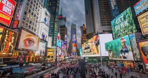 Une rue animée en milieu urbain, avec de hauts immeubles, des panneaux publicitaires et des piétons.