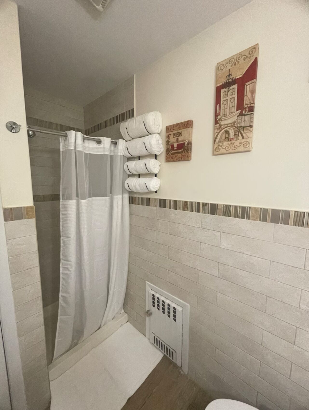 Une salle de bain avec une douche, un porte-serviettes avec des serviettes et deux œuvres d’art accrochées au mur.