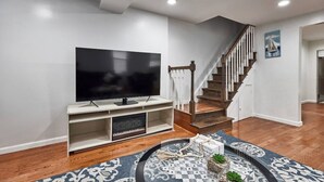A living room with a flat-screen TV on a stand, a staircase with wooden steps, and a patterned rug. - Cool- Private-Entire House-Near NYC-EWR/Free Parking-3beds/2bath (Bayonne)