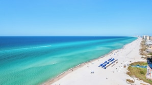 Una playa con aguas turquesas cristalinas, una orilla arenosa y una fila de sombrillas azules.