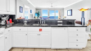 Una cocina moderna con armarios blancos, una encimera negra y vista al océano a través de grandes puertas correderas.