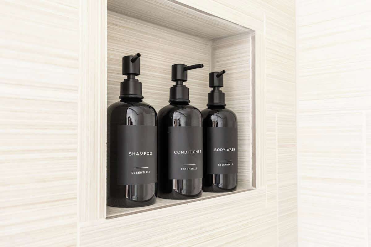 A shelf with three black bottles labeled 'Shampoo Essentials,' 'Conditioner Essentials,' and 'Body Wash Essentials.'