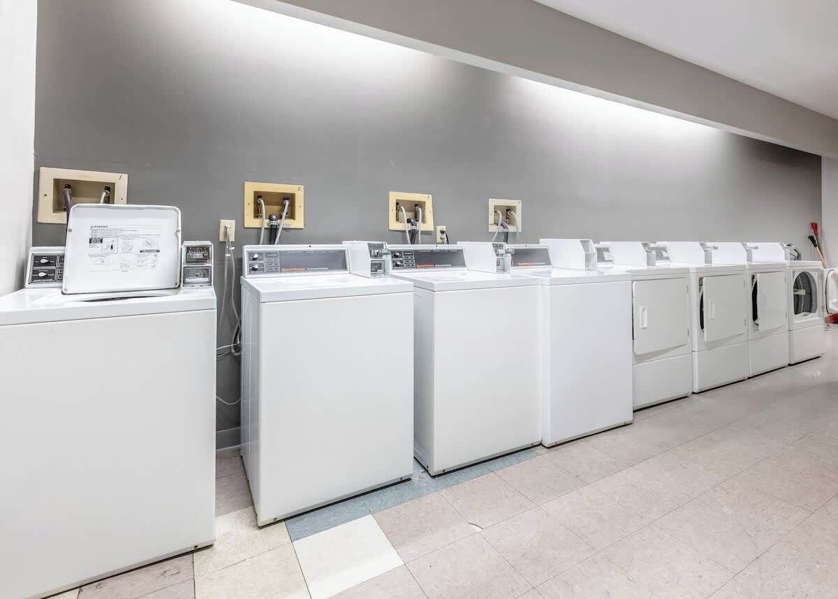 A row of white laundry machines in a modern, clean facility with grey walls and a tiled floor.