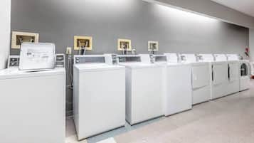 A row of white laundry machines in a modern, clean facility with grey walls and a tiled floor.