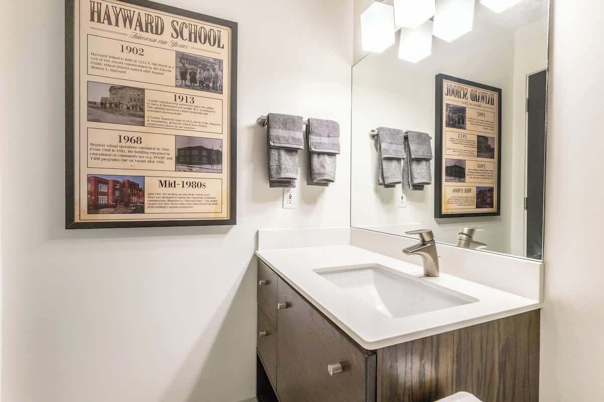 Une salle de bain avec une frise chronologique encadrée retraçant des événements historiques, un lavabo, un miroir et des serviettes.