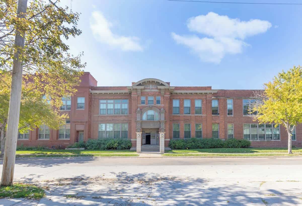 A large brick building with a central entrance, surrounded by trees and a clear sky.