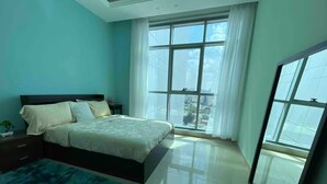 A bedroom with a bed, a nightstand, a blue rug, and large windows with curtains.