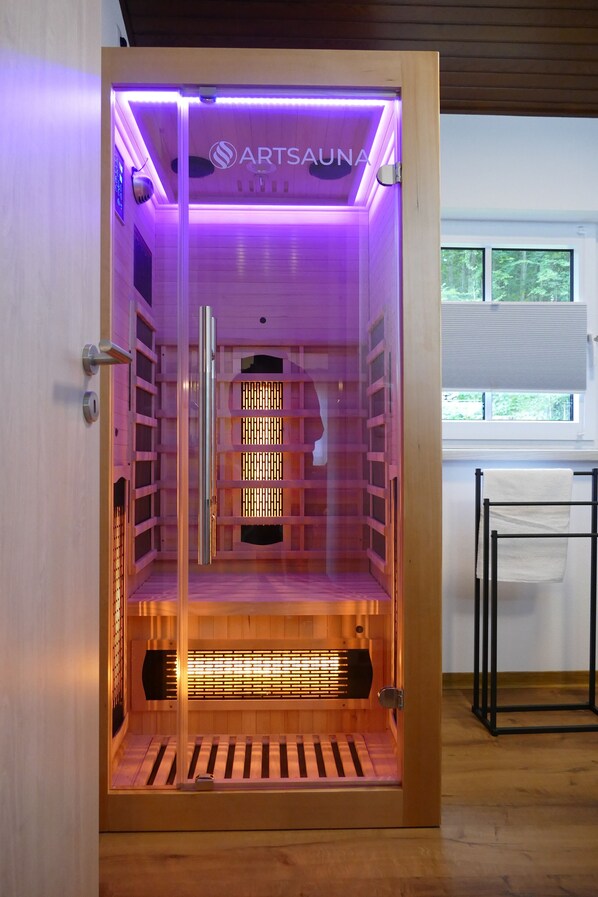 A sauna with a wooden interior, a glass door, and a sign reading 'ARTSAUNA.'