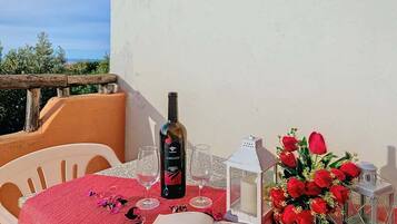 Un tavolo apparecchiato con una bottiglia di vino, bicchieri, un libro e un bouquet di rose rosse su un balcone con vista.