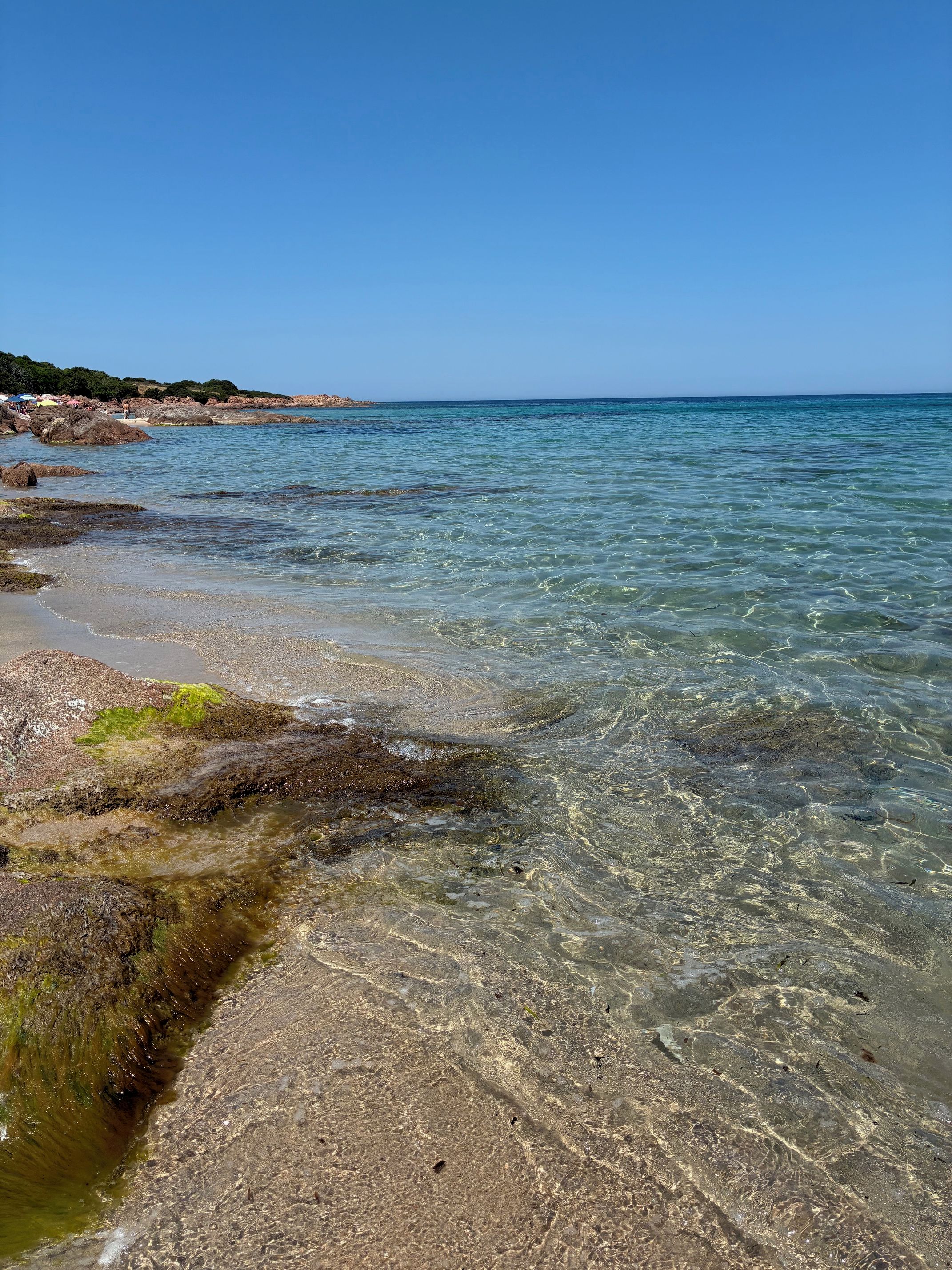 A clear coastal beach with rocky shoreline and calm sea.