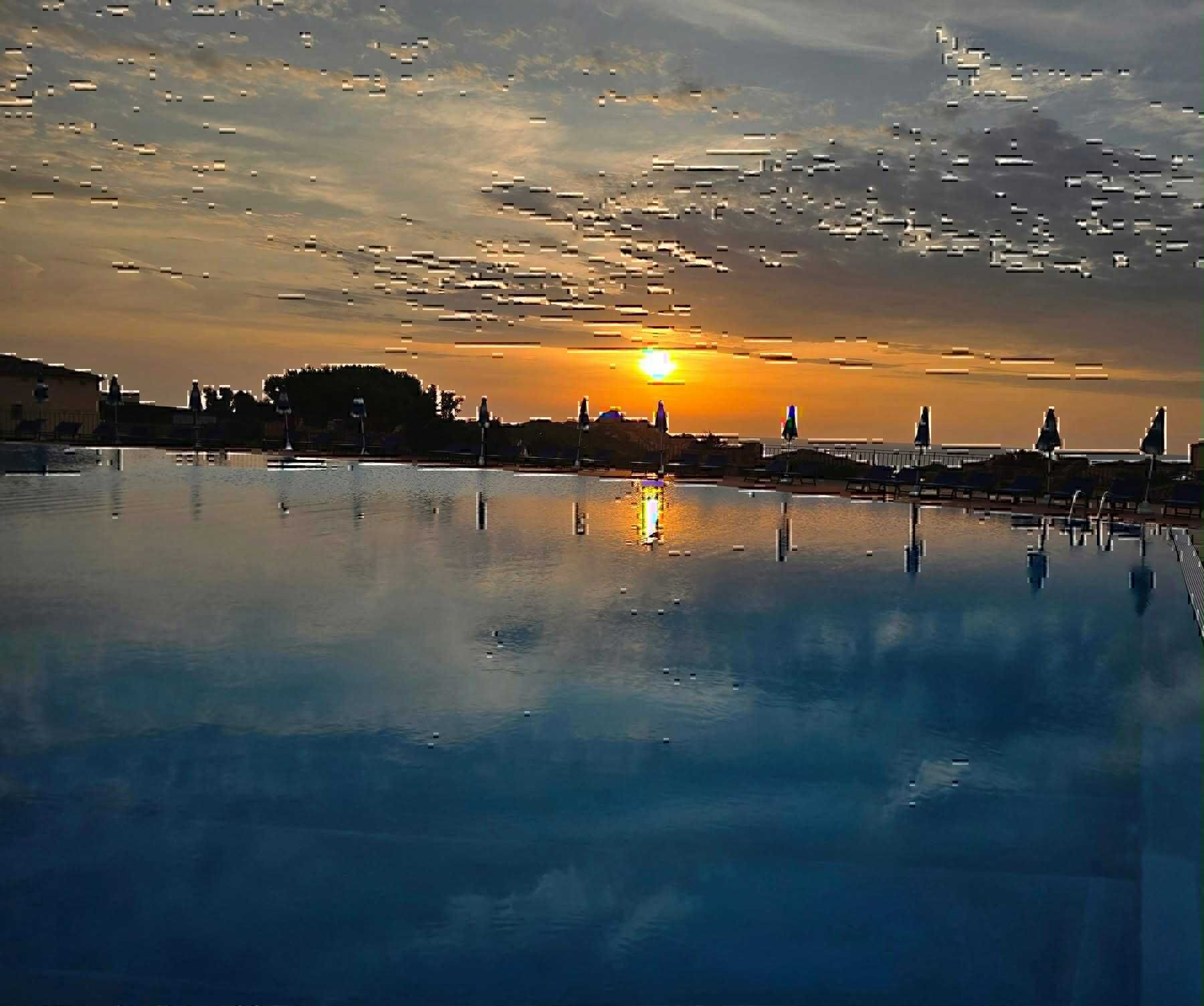 Un tramonto su un'acqua calma, con un molo e poltrone da relax.