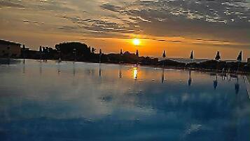 Un tramonto su un'acqua calma, con un molo e poltrone da relax.