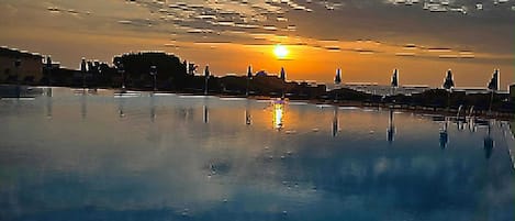 A sunset over a calm body of water with a pier and lounge chairs.