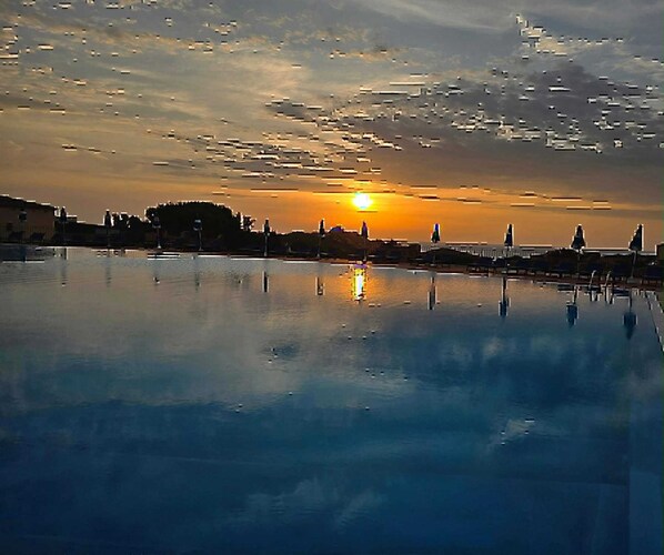 Ein Sonnenuntergang über ruhigem Wasser mit einem Steg und Liegestühlen.