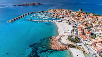 Una vista aerea di una cittadina costiera con un porto turistico, spiaggia sabbiosa e edifici storici.