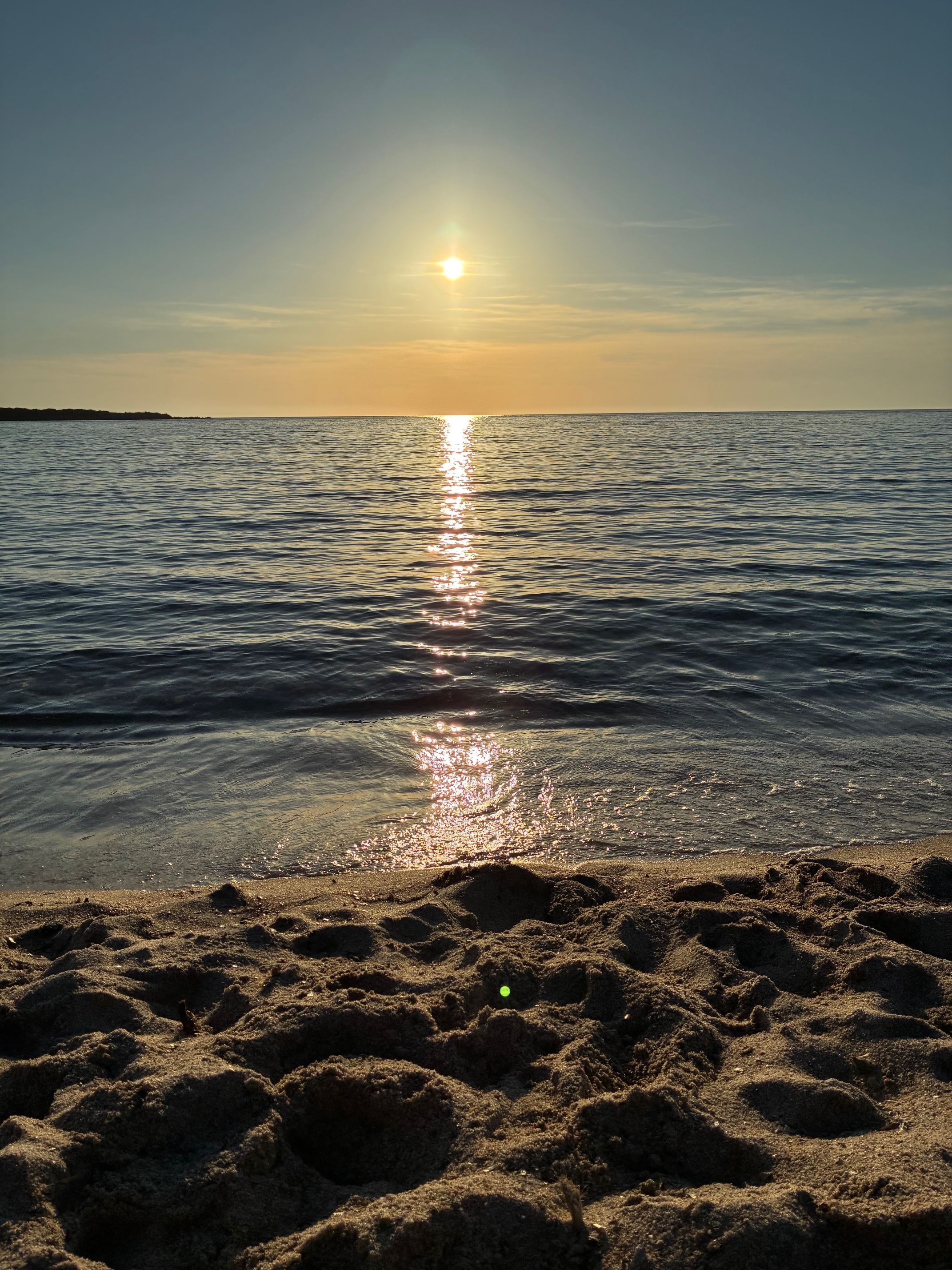A beach with a clear sky and the sun reflecting on the water.