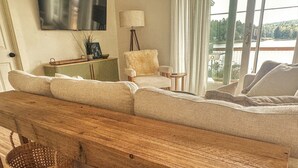 A cozy living room with a wooden bench, a fluffy chair, and a view of a lake through large windows.