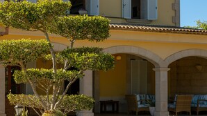 A building with a yellow facade, white shutters, and a covered patio with outdoor seating. - Fantastic finca with a large pool and just a few steps from Alcúdia's old town (Alcúdia)