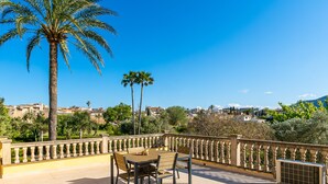 A terrace with a wooden table and chairs, a palm tree, and a view of a town. - Fantastic finca with a large pool and just a few steps from Alcúdia's old town (Alcúdia)