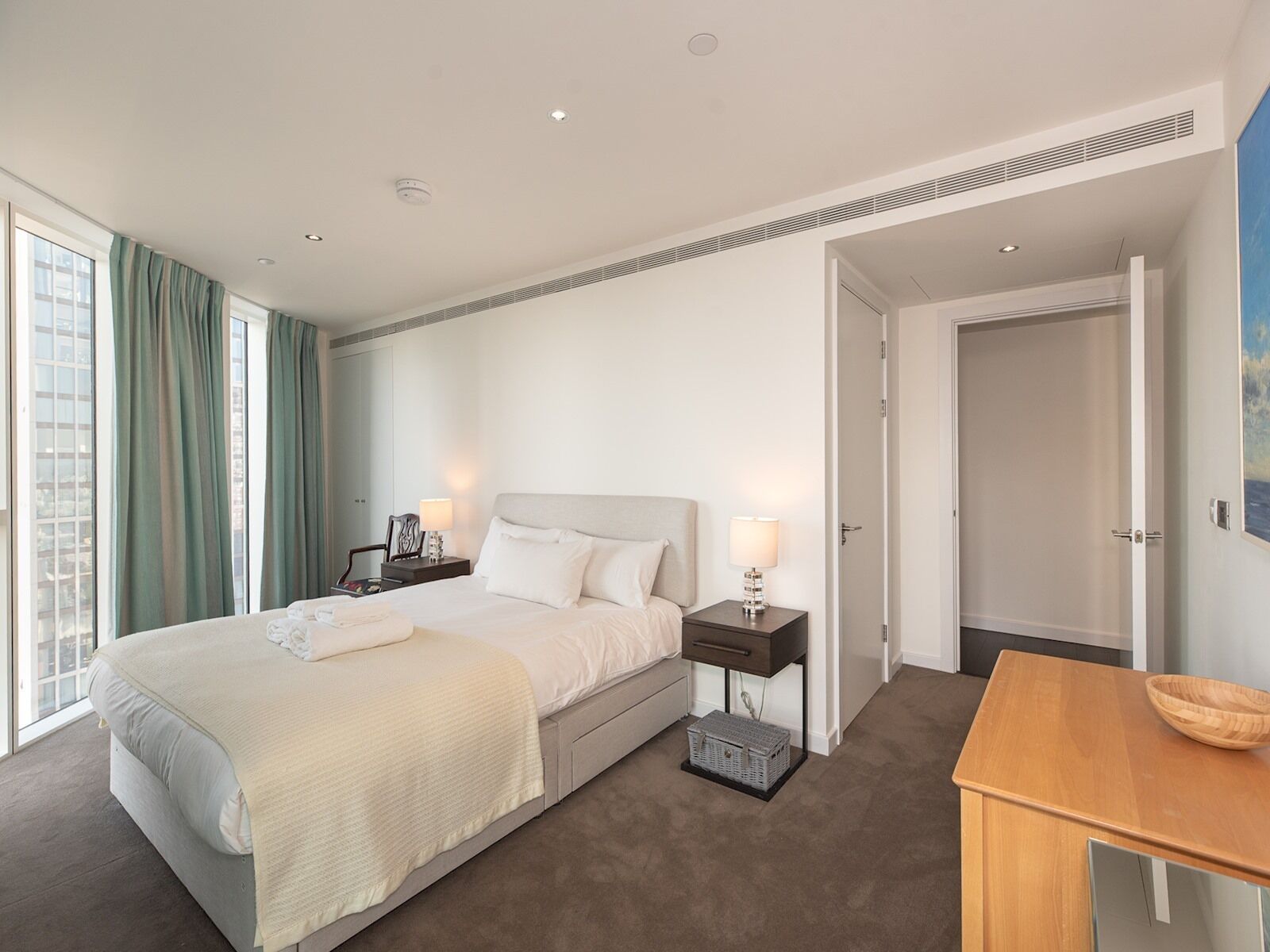 Ein modernes Hotelzimmer mit einem großen Bett, Nachttischen, einem Holztisch und Blick auf die Stadt durch große Fenster.