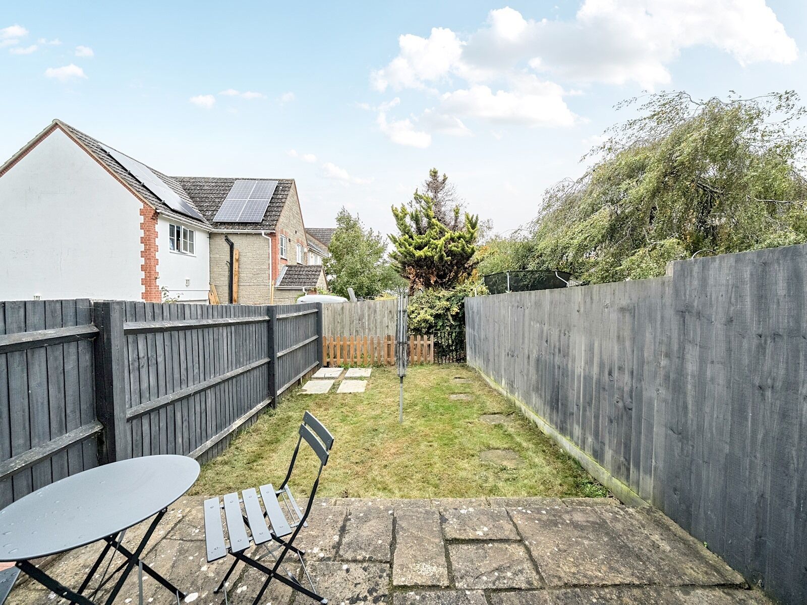 A backyard with a patio table and chairs, a wooden fence, and a house in the background.