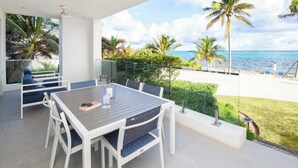 Un balcon avec une table et des chaises, donnant sur une plage bordée de palmiers et sur l’océan.