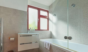 A bathroom with a bathtub, a window, a towel, and a toilet.