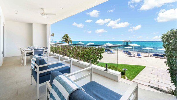 Un balcón con vista a la playa, mobiliario exterior y sombrillas.